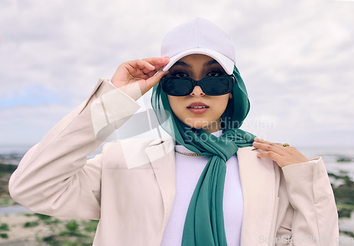 Image of Portrait, fashion or sunglasses with a saudi woman outdoor in a cap and scarf for contemporary style. Islam, face and hijab with a trendy young muslim or arab person posing outside in modern clothes