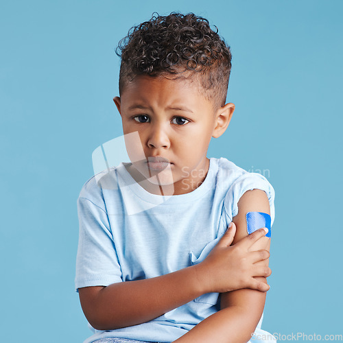 Image of Portrait, sad and kid with arm bandage in studio isolated on a blue background. Face, upset and child with plaster after vaccine, injury or wound for healthcare wellness, first aid or medical help.