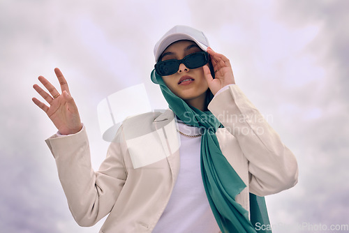 Image of Portrait, fashion or religion with a muslim woman on a cloudy sky background in a cap and scarf for modern style. Islam, faith or hijab with a trendy young arab person outside in contemporary clothes