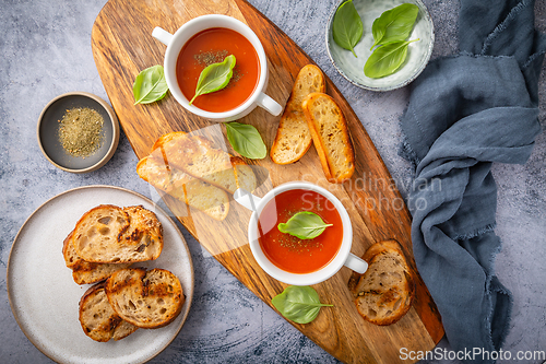 Image of Homemade tomato soup with basil, toast and olive oil on a wooden cutting board. 