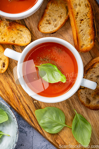 Image of Homemade tomato soup with basil, toast and olive oil on a wooden