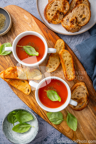 Image of Homemade tomato soup with basil, toast and olive oil on a wooden cutting board. 