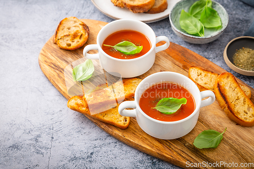 Image of Homemade tomato soup with basil, toast and olive oil on a wooden