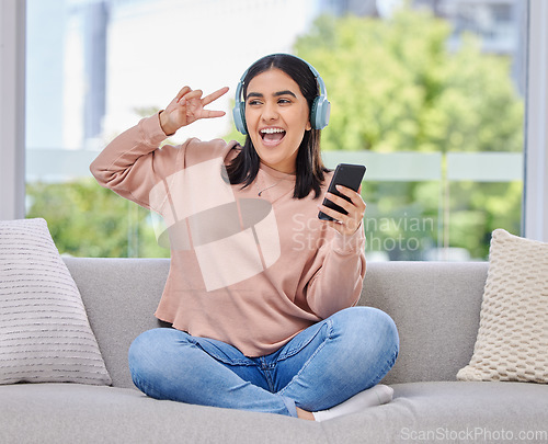 Image of Woman, headphones and smartphone for singing on sofa for happiness, relax and music in home living room. Girl, phone and audio streaming subscription for hip hop, rock or edm with peace sign in house