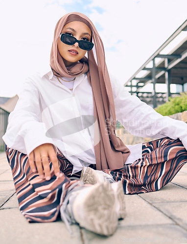 Image of Portrait, fashion or tradition with a muslim woman outdoor in sunglasses and a scarf for contemporary style. Islam, faith or hijab with a trendy young islamic person sitting outside in modern clothes