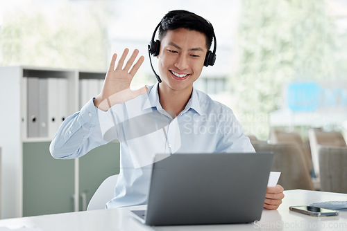 Image of Asian man, laptop and video call in call center, customer service or virtual assistant at the office. Happy male person or consultant agent waving hello on computer for online advice at the workplace