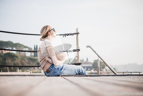 Image of Mother breast feeding her little baby boy infant child on old wooden pier by the sea on nice warm spring day enjoing nature and warm breeze outdoors.