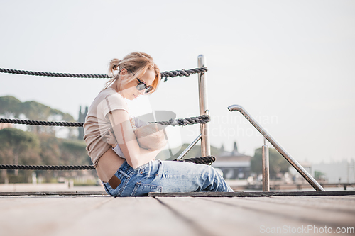 Image of Mother breast feeding her little baby boy infant child on old wooden pier by the sea on nice warm spring day enjoing nature and warm breeze outdoors.