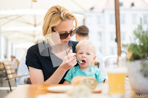 Image of Young mother relaxing together with her little child, adorable toddler girl, in summer outdoors cafe drinking coffee and eating muffin or cupcke. Family in love. Kid an beautiful woman.