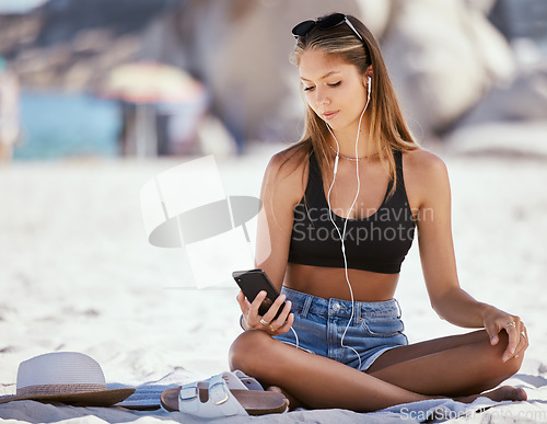 Image of Phone, music and a woman on the beach in summer to relax while on holiday or vacation by the ocean. Sand, nature and mobile with an attractive young female traveler sitting on the coast as a tourist