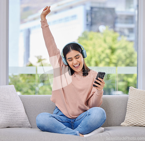 Image of Woman, excited and phone with headphones for music on a home sofa with happiness and energy. Happy female person on a lounge couch with a smartphone for streaming or listen to audio, podcast or radio