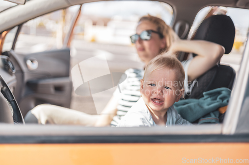 Image of Mother and her infant baby boy child on family summer travel road trip, sitting at dad's front seat, waiting in the car for father to buy farry tickets.