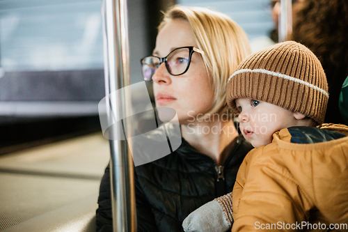 Image of Mother carries her child while standing and holding on to the bus. Mom holding her infant baby boy in her arms while riding in a public transportation. Cute toddler boy traveling with his mother.