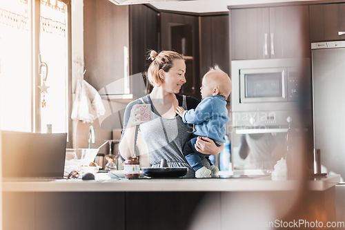 Image of Happy mother and little infant baby boy together making pancakes for breakfast in domestic kitchen. Family, lifestyle, domestic life, food, healthy eating and people concept.