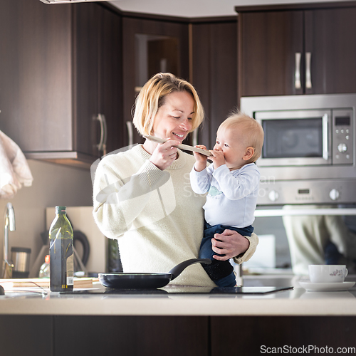 Image of Happy mother and little infant baby boy cooking and tasting healthy dinner in domestic kitchen. Family, lifestyle, domestic life, food, healthy eating and people concept.