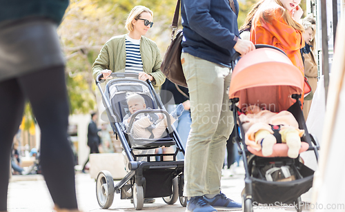 Image of Mother walking and pushing his infant baby boy child in stroller in crowd of people wisiting sunday flea market in Malaga, Spain.