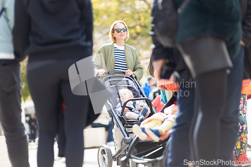 Image of Mother walking and pushing his infant baby boy child in stroller in crowd of people wisiting sunday flea market in Malaga, Spain.