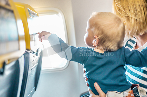 Image of Mom and child flying by plane. Mother holding and playing with her infant baby boy child in her lap during economy comercial flight. Concept photo of air travel with baby. Real people.