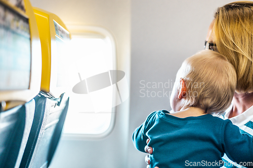 Image of Mom and child flying by plane. Mother holding and playing with her infant baby boy child in her lap during economy comercial flight. Concept photo of air travel with baby. Real people.