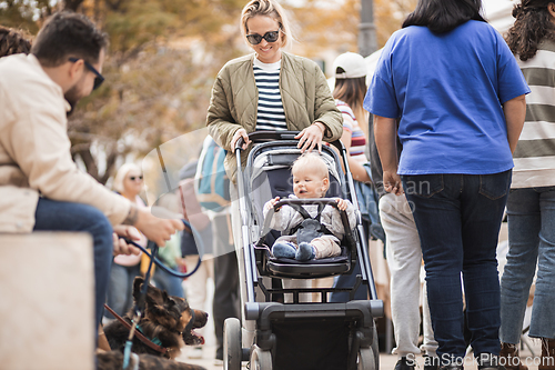 Image of Mother walking and pushing his infant baby boy child in stroller in crowd of people wisiting sunday flea market in Malaga, Spain.