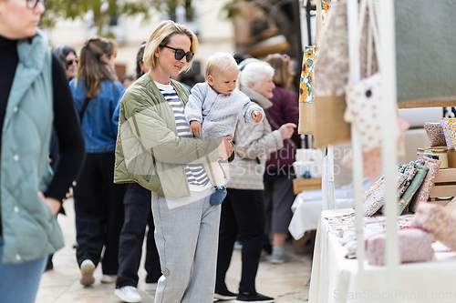 Image of Mother walking carrying his infant baby boy child in crowd of people wisiting sunday flea market in Malaga, Spain