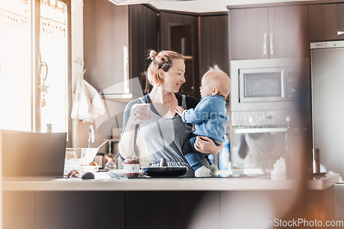 Image of Happy mother and little infant baby boy together making pancakes for breakfast in domestic kitchen. Family, lifestyle, domestic life, food, healthy eating and people concept.