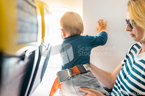 Image of Mom and child flying by plane. Mother holding and playing with her infant baby boy child in her lap during economy comercial flight. Concept photo of air travel with baby. Real people.