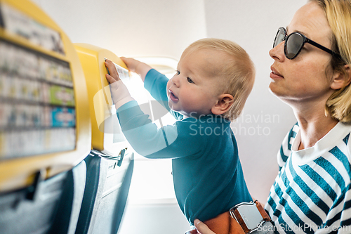 Image of Mom and child flying by plane. Mother holding and playing with her infant baby boy child in her lap during economy comercial flight. Concept photo of air travel with baby. Real people.