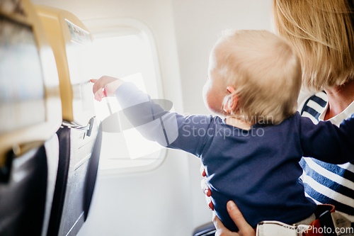 Image of Mom and child flying by plane. Mother holding and playing with her infant baby boy child in her lap during economy comercial flight. Concept photo of air travel with baby. Real people.