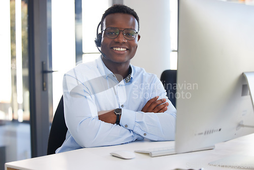 Image of Arms crossed, portrait and a black man at a desk in a call center for online support and service. Smile, pride and an African customer care employee at a computer for telemarketing or sales help