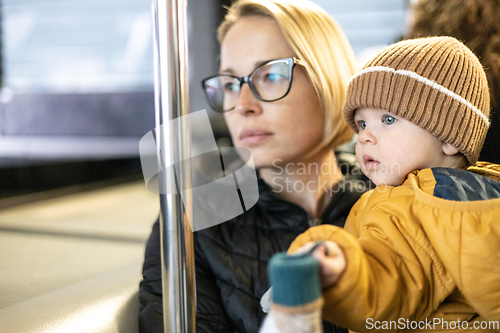 Image of Mother carries her child while standing and holding on to the bus. Mom holding her infant baby boy in her arms while riding in a public transportation. Cute toddler boy traveling with his mother.