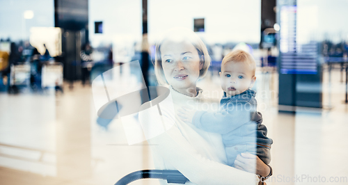 Image of Thoughtful young mother looking trough window holding his infant baby boy child while waiting to board an airplane at airport terminal departure gates. Travel with baby concept.