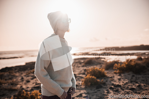 Image of Portrait of young stylish woman wearing wool sweater, wool cap and sunglasses on long sandy beach in spring