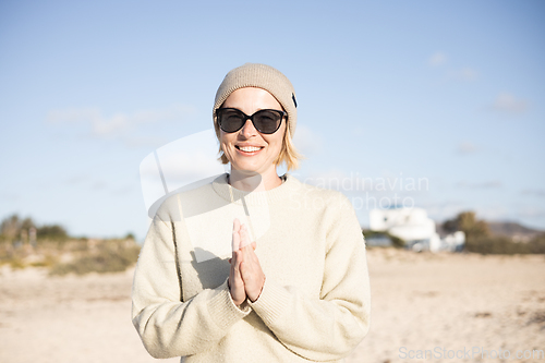 Image of Portrait of young stylish woman wearing wool sweater, wool cap and sunglasses on long sandy beach in spring