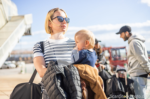 Image of Motherat travelling with his infant baby boy child. Mom holding travel bag and her infant baby boy child while queuing for bus in front of airport terminal station.