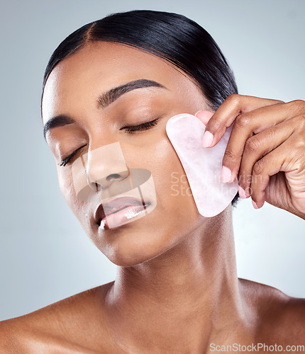 Image of Beauty, facial and gua sha with face of woman in studio for massage, wellness and cosmetics. Spa, self care and glow with model on grey background for skincare, cosmetology and rose quartz crystal