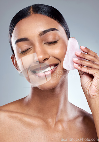 Image of Beauty, smile and gua sha with face of woman in studio for massage, wellness and cosmetics. Spa, self care and glow with model on grey background for facial, cosmetology and rose quartz crystal
