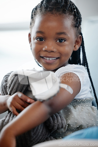 Image of African girl kid, vaccine and portrait with smile, medicine or happiness on sofa for wellness in hospital. Female child, happy or excited with plaster for injection, healthcare or brave to stop virus