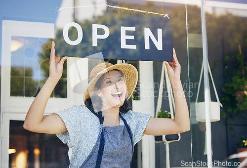 Image of Portrait, plant nursery and open with a woman hanging a sign in the window of her shop for gardening. Small business, garden center and an excited young female florist opening her new flower store