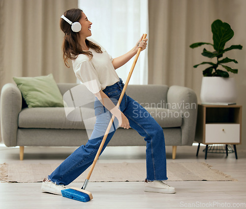 Image of Woman, singer and broom to clean living room with funny dance, sweeping floor and rock performance in home. Girl, comic singing and cleaner with spring cleaning, music and headphones for guitar solo