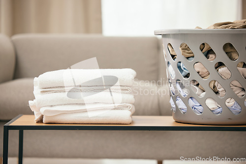 Image of Clean laundry, table and basket in home living room for folding, hospitality and housekeeping. Towel stack, plastic bucket and spring cleaning service for fabric, clothes and hygiene on desk in house