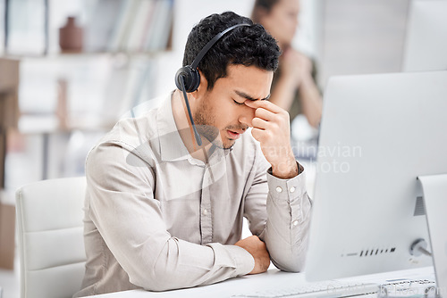 Image of Mental health, man with headache and headset at his desk with computer in a modern workplace office. Telemarketing or call center, sad or burnout and male person tired or depressed at his workstation