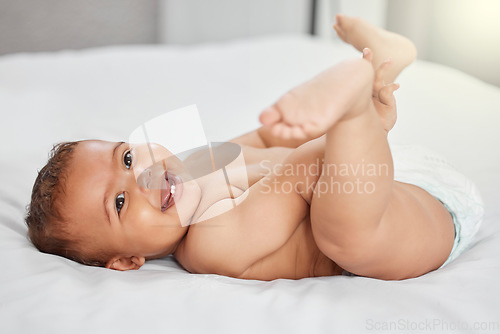 Image of Baby, funny and child play with feet on bed in home having fun and enjoying time alone. Happy, newborn and playing with foot, toes and cute infant, kid or toddler with growth, development and relax