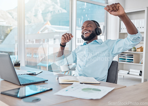 Image of Happy black man at desk with headphones, music and enjoying work with excited dance at desk with tech. African businessman in modern office with earphones, dancing and fun working on startup report.