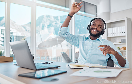 Image of Dance, happy man at desk with headphones, music and enjoying work with online radio streaming service. African businessman in modern office with earphones, dancing and fun working on startup report.