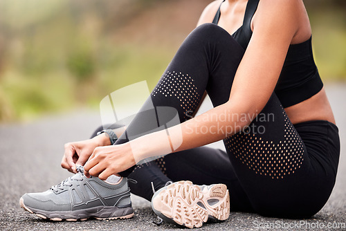 Image of Fitness, woman tying sneakers and sitting on road for safety during outdoor marathon training. Running, cardio health and wellness, female athlete fixing laces on footwear and runner shoes on asphalt