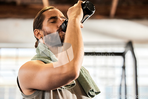 Image of Tired, break and a man drinking water in the gym after training, hydrating and thirsty after a workout. Fitness, health and a hydrated person with a bottle to drink after sports, cardio or exercise