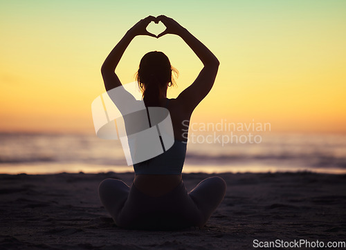 Image of Woman yoga, heart hand and shadow at sunset at beach and ocean with peace and zen hands sign. Silhouette, nature and sea on a vacation with calm meditation and love emoji gesture outdoor at sunrise