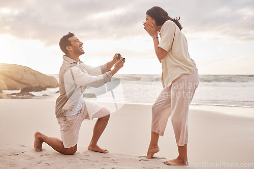 Image of Couple, engagement proposal and surprise at beach with smile, happiness or love on vacation in sunset. Man, woman and ring with marriage offer by ocean with smile, excited face or together on holiday