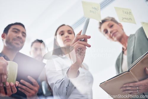 Image of Teamwork, writing and business people on glass board for planning, brainstorming and schedule or workflow notes. Notebook, tablet and women, men or group with sticky note ideas, solution and window